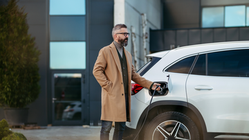 Mann in Mantel laedt E-Auto